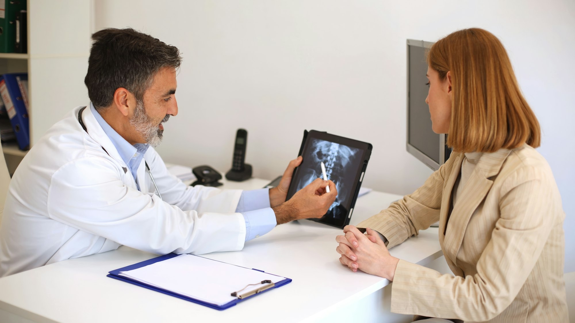 Doctor consulting patient with spine X-ray on tablet in a medical office setting
