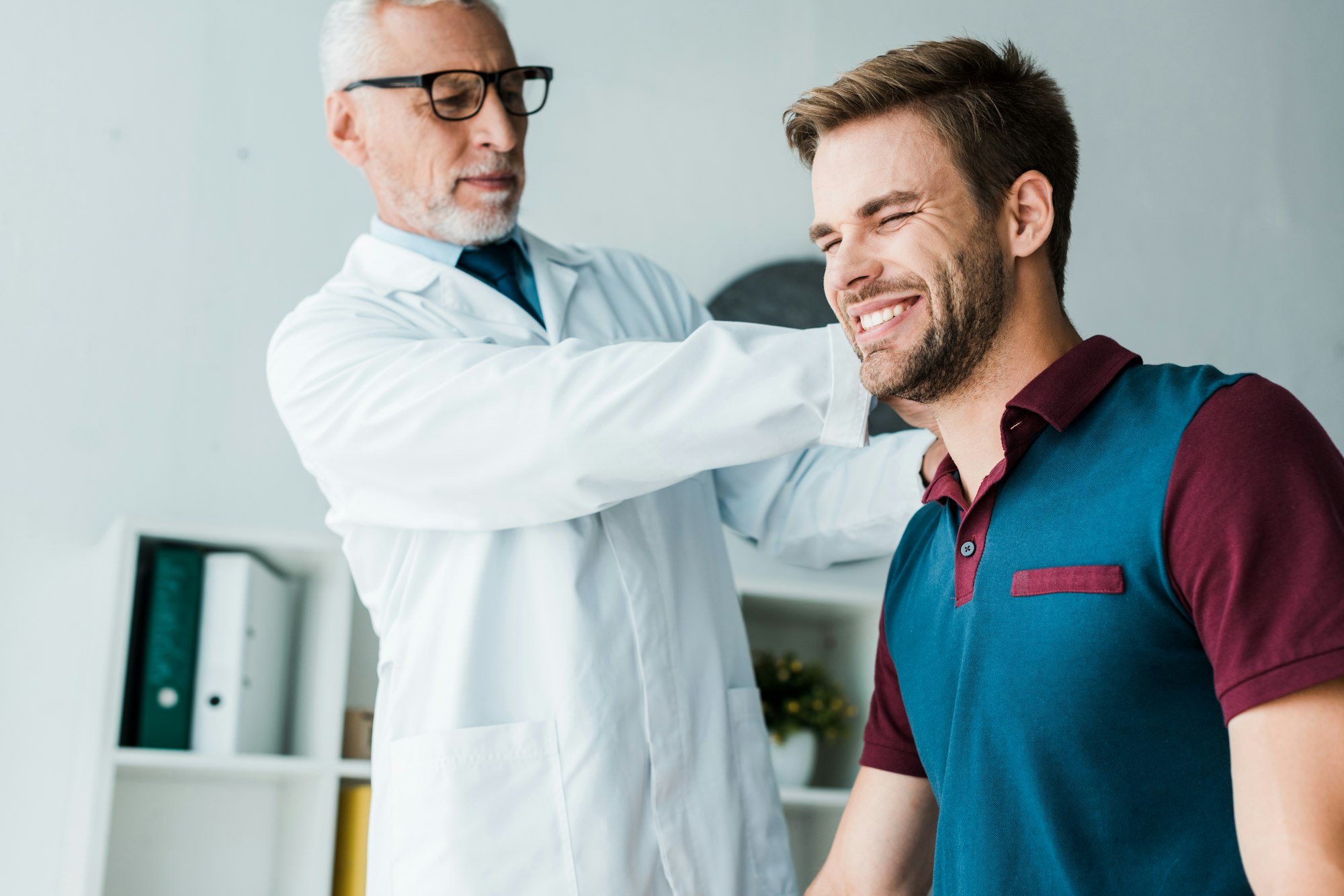 chiropractor in white coat and glasses touching happy patient in clinic