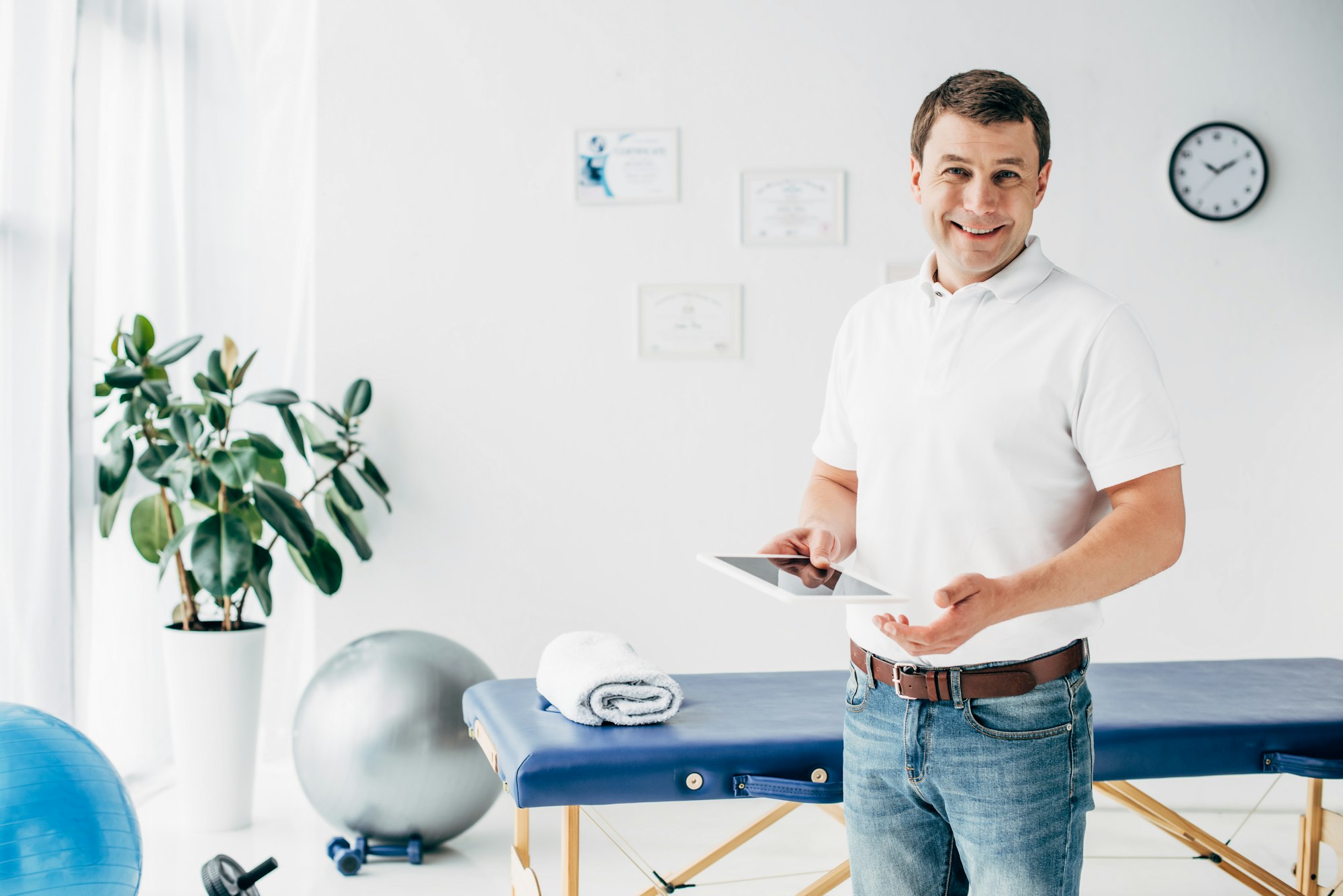 smiling chiropractor holding Digital Tablet in hospital and looking at camera